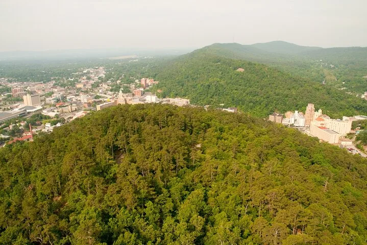 Eine Luftaufnahme eines bewaldeten Hügels mit Blick auf eine im Tal eingebettete Stadt.